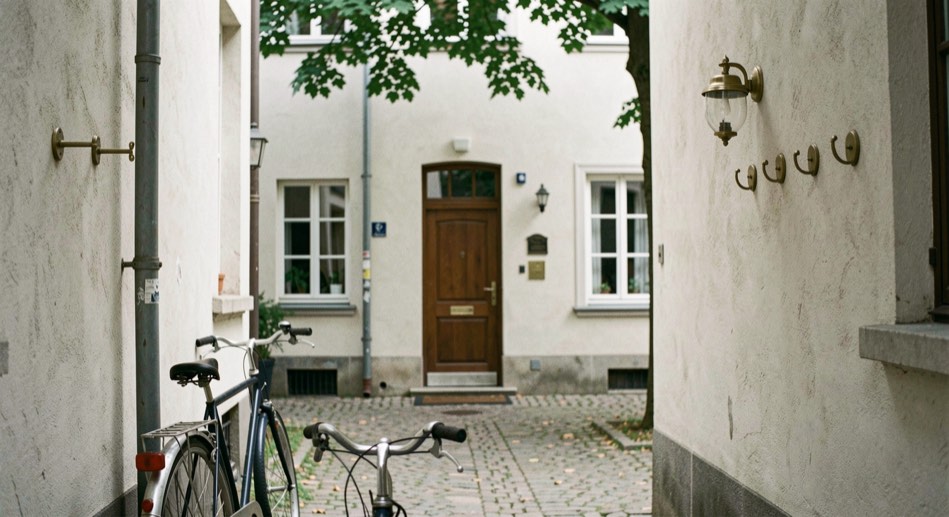 Quiet Viennese courtyard entrance of a small pension with a brass door bell row, bicycle leaning on plaster walls and plane trees overhead